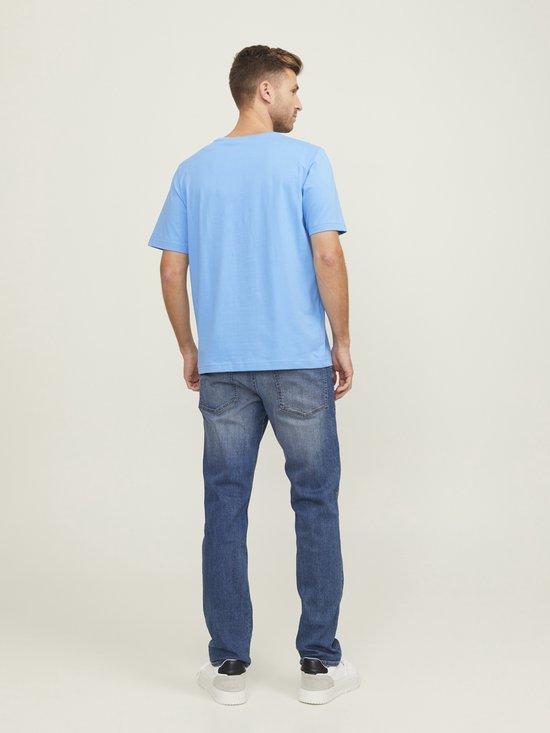 Man met blauwe T-shirt en spijkerbroek, staand met de rug naar de camera.