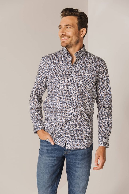 Man met hand in broekzak draagt een blauw overhemd met een fijn wit, bruin en donkerblauw patroon.