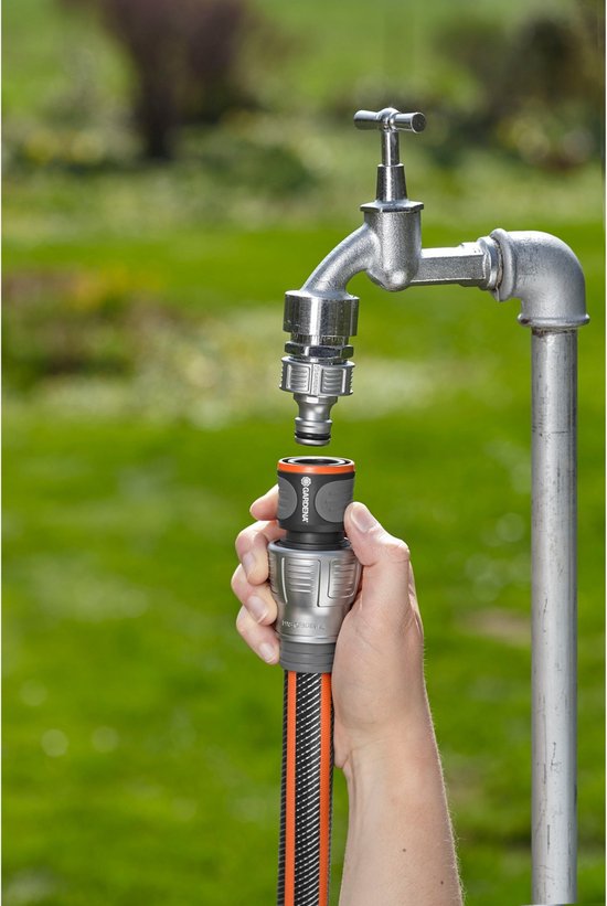Hand bevestigt een grijze en zwarte Gardena slangkoppeling met oranje accenten aan een kraan.