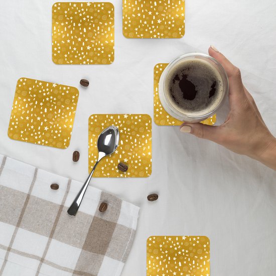 Une main tenant une tasse de café au-dessus d'un sous-verre doré à motif de Noël blanc.