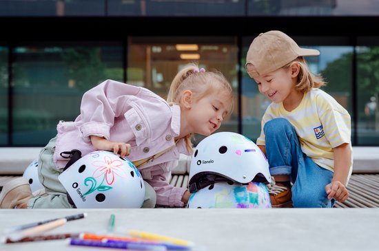 Twee kinderen bekijken helmen, één met bloemenprint en één met gekleurde krabbels.