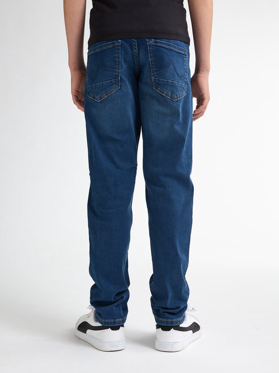 Jongen in een blauwe jeans en witte sneakers, gezien vanaf de achterkant.