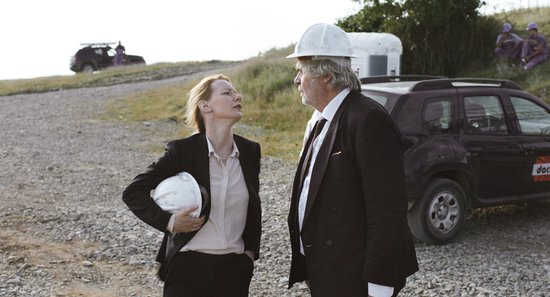 Een man met een wit helm en een pak staat tegenover een vrouw in een zwart pak met een witte blouse, die een witte helm vasthoudt.
