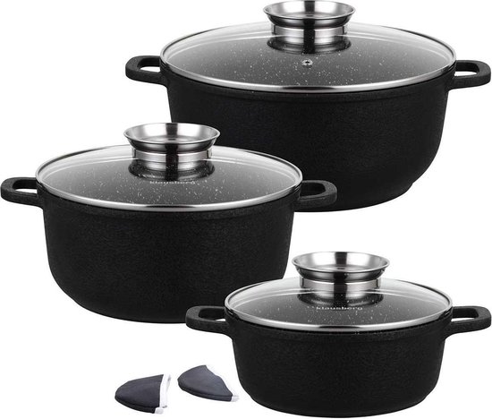 Trois casseroles noires avec couvercles en verre et poignées, avec deux dessous de plat en tissu.