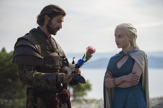 Een man in harnas geeft een vrouw in blauwe jurk een bloem met blauwe en rode blaadjes.