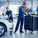 Mannelijke en vrouwelijke automonteurs in een garage, die werken aan een auto met de motorkap open.
