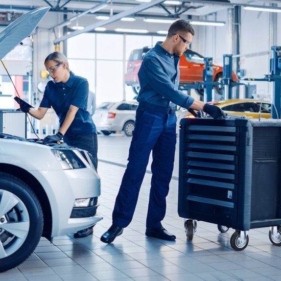 Mannelijke en vrouwelijke automonteurs in een garage, die werken aan een auto met de motorkap open.