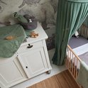 Babykamer met commode met daarop een groene badcape, borstel en houten speelgoed. Naast de commode een wieg.