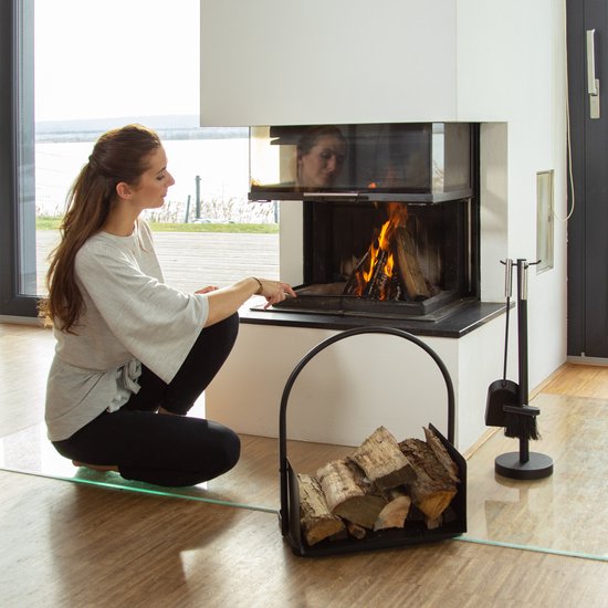 Vrouw bij open haard met zwarte metalen houtmand gevuld met hout.