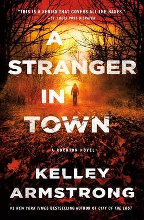 Boekomslag: "A Stranger in Town" van Kelley Armstrong. Een figuur staat op een bosweg bij zonsondergang. Tekst: "A STRANGER IN TOWN".