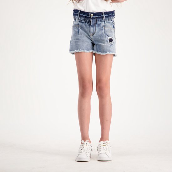 Meisje in een blauwe denim short met gerafelde zoom, scheurdetails en ruches tailleband.