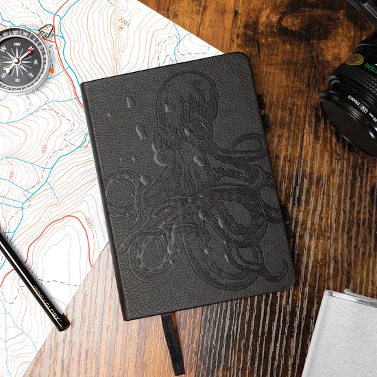 Gesloten zwart notitieboek met een reliëfprint van een octopus op de voorkant. Geplaatst op een landkaart met een kompas.