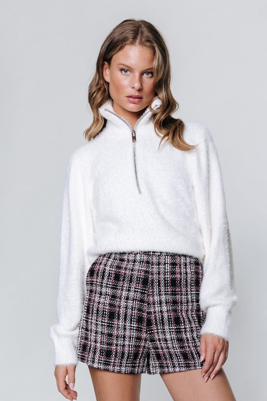 Model in een korte broek met roze, zwarte en witte ruit en een geborduurd effect, gecombineerd met een witte trui.