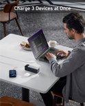 Man laadt laptop, telefoon en oortjes op met de Anker powerbank aan een tafel.