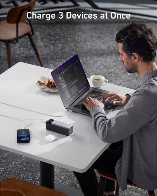 Man laadt laptop, telefoon en oortjes op met de Anker powerbank aan een tafel.