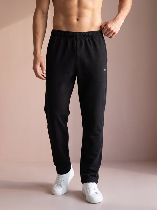 Zwarte lange sportbroek met logo op de linkerheup, gedragen door een man met witte sneakers.