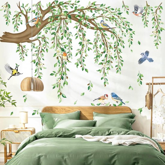 Muursticker van een bruine boomtak met groene bladeren en bloesems, boven een groen bed, met diverse zangvogels en een lamp.
