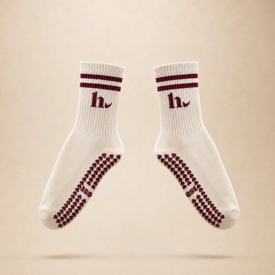 Une paire de chaussettes blanc cassé avec des rayures bordeaux sur le revers et un motif cœur sur la semelle. Un logo 'h' bordeaux également.