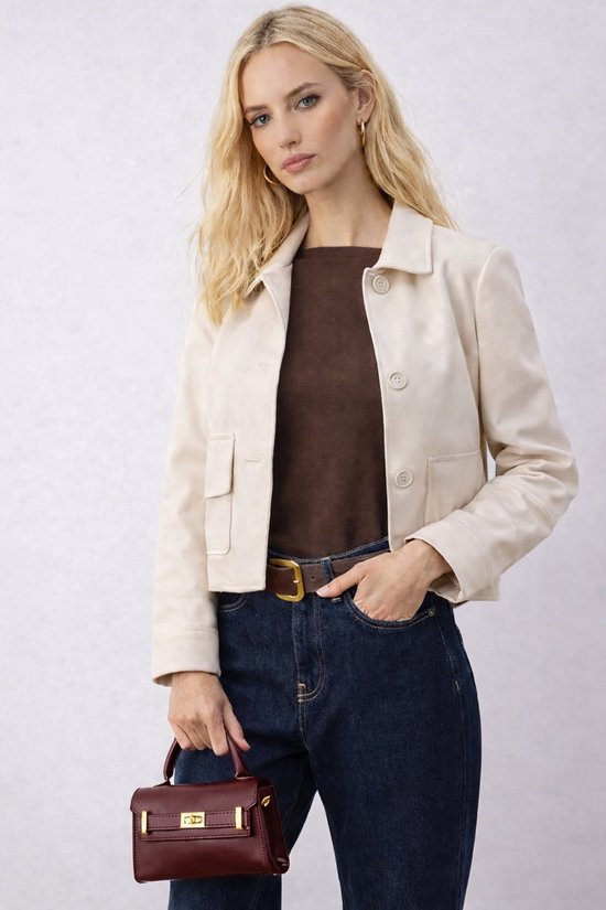Model met beige blazer, bruine top, jeans en bordeauxrode handtas.
