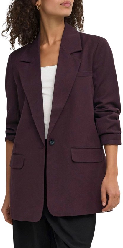 Een vrouw draagt een paarse oversized blazer, een witte top en zwarte wijde broek. De blazer heeft grote revers.