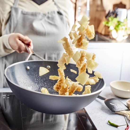Persoon bakt gefrituurde stukken in een wokpan.