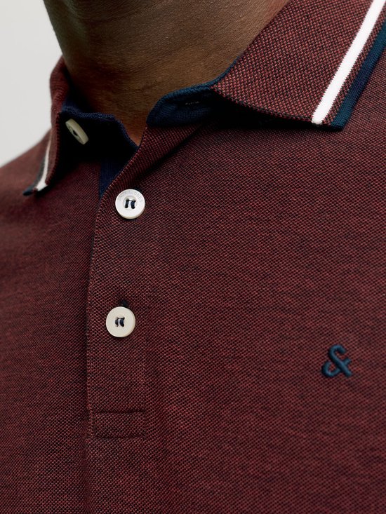 Close-up van de kraag en knopen van een donkerrode polo met logo.