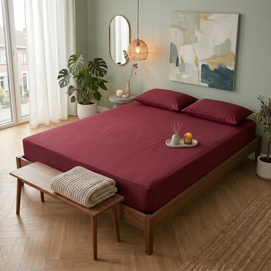 Une chambre avec un lit double fait avec un drap-housse bordeaux et des oreillers.