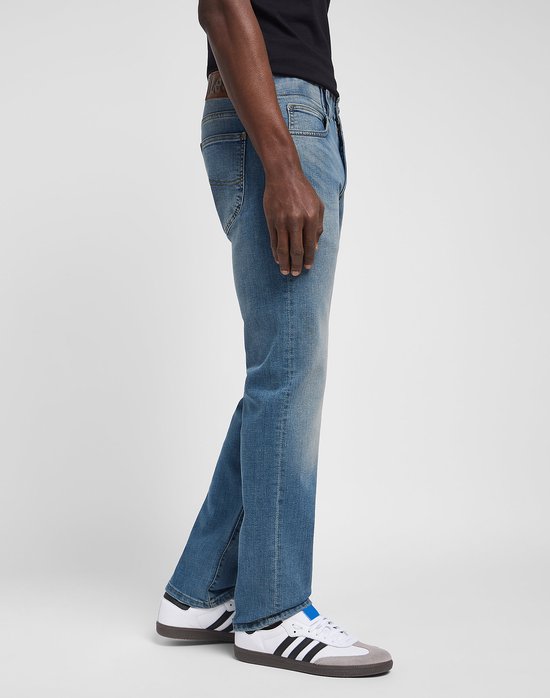 Profiel van een man die een lichtblauwe spijkerbroek draagt met omgeslagen broekspijpen, witte sneakers met blauwe accenten.
