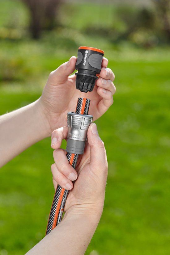 Handen koppelen een Gardena slang met oranje strepen aan een zilverkleurige koppeling.