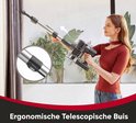 Vrouw met rode top en jeans verstelt de ergonomische, telescopische buis van de stofzuiger.