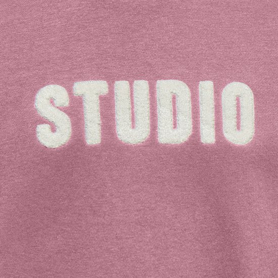 Detail van de witte 'STUDIO' tekst op een roze sweater.