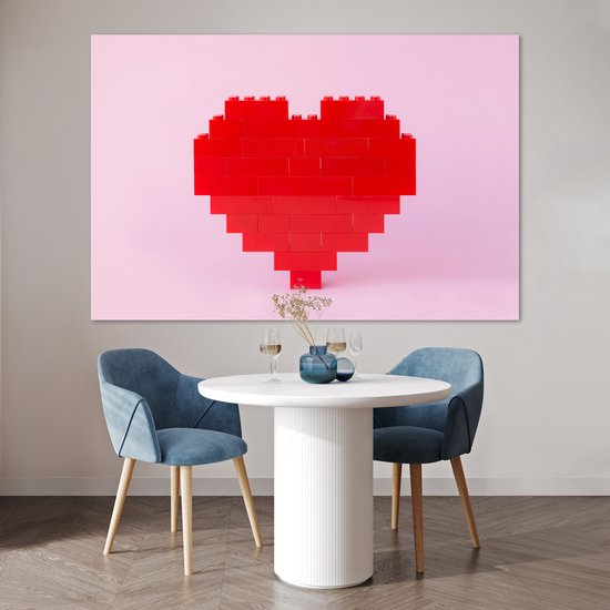 Rood hart van bouwblokken op een roze achtergrond, boven een witte tafel met twee blauwe stoelen.