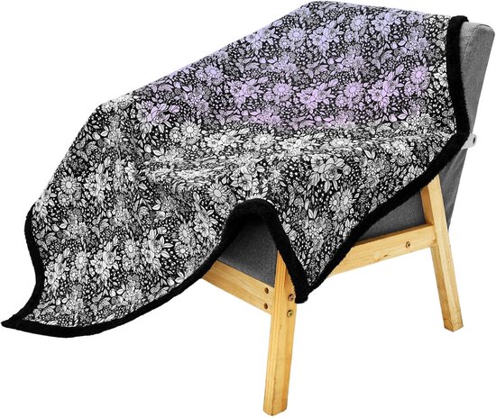 Grijze fauteuil met een deken met bloemenpatroon erop. De deken is zwart met witte bloemen en heeft een zwarte pluizige rand.