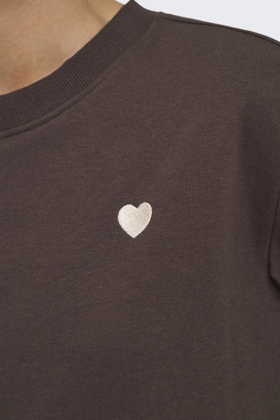 Detailopname van het geborduurde beige hartje op de bruine sweater.