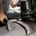 Close-up van een grijze autostoel waar een reinigingsmondstuk een vlek verwijdert.