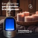 Aroma diffuser met zilveren voet, donkere glazen kap met blauwe gloed. Witte kaarsen op de achtergrond.