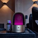 Aroma diffuser met zilveren voet, donkere kap, paarse verlichting en een flesje geurolie op een marmeren dienblad.