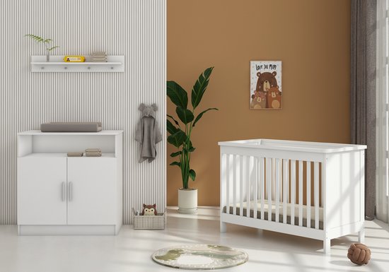 Witte babykamer met wit bed, witte commode, een teddybeer poster, plant, speelgoedmand en ronde mat.
