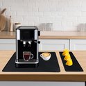 Zwarte koffiebarmat met een zilverkleurige espressomachine, een kop cappuccino, drie gele kopjes en een glas espresso.