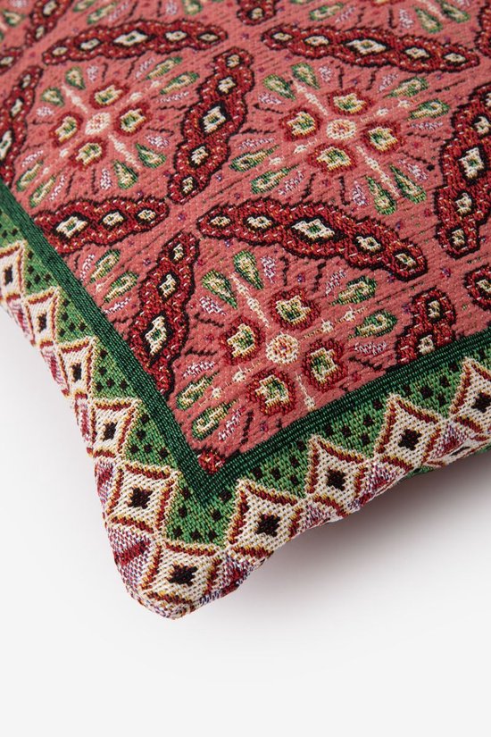 Detail van een kussen met mozaïekprint. Rood, groen, beige en paarse patronen met groene bies.