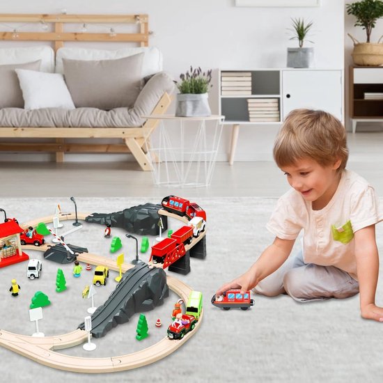 Jongen speelt met een houten treinbaan met rode treinen, bruggen en tunnels.