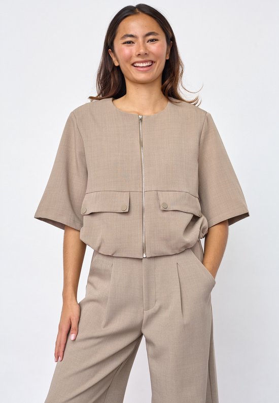 Model draagt beige gilet met ritssluiting, twee klepzakken en broek.