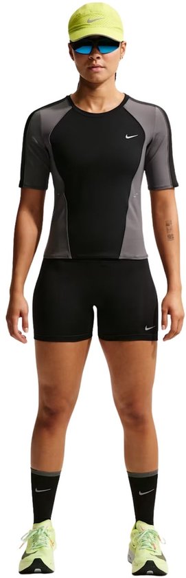 Vrouw in zwart-grijze Nike hardloopset met zwarte short en fluor-gele pet.