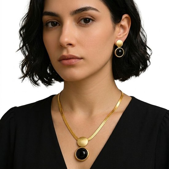 Gros plan d'une femme aux cheveux courts et noirs, portant un collier doré avec pendentif noir et boucles d'oreilles.