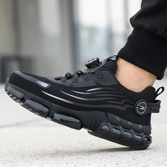 Homme portant une chaussure de travail noire avec fermeture rotative et rayures argentées, sur fond clair.