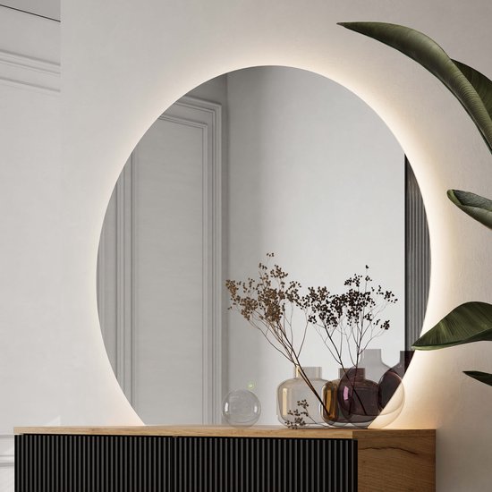 Halfronde LED-spiegel boven een houten dressoir met vazen en een grote kamerplant.