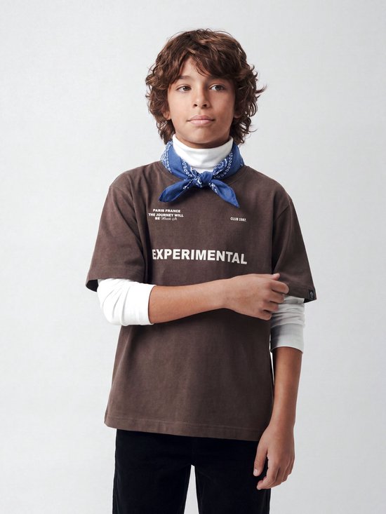 Jongen met bruin t-shirt met tekst 'EXPERIMENTAL', witte coltrui en blauwe bandana.