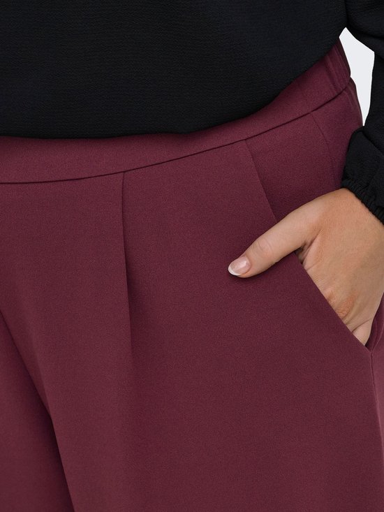Gedetailleerde close-up van de bordeauxrode stof van een wijde broek met plooien en een zak.