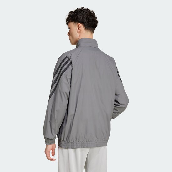 Achterkant van een grijs Adidas trainingsjack met zwarte 3-strepen op de mouwen.