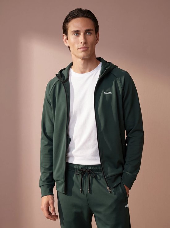 Model draagt een donkergroene hoodie met rits en witte tekst op de borst, met bijpassende joggingbroek.